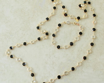 May include: A gold-tone chain necklace and matching bracelet set featuring alternating round black and clear faceted stones set in metal bezels. The jewelry pieces are arranged in a circular and linear pattern on a light surface.
