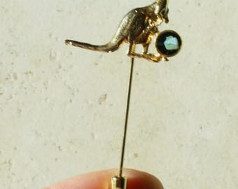 May include: A gold-toned metal stick pin featuring a kangaroo figure. The kangaroo is depicted in a standing position with a small, round, dark iridescent stone set into the area where a joey would be located in the pouch.