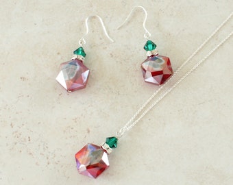 May include: A jewelry set consisting of a necklace and two drop earrings. Each piece features a faceted, hexagonal red and iridescent crystal bead topped with a small green crystal bead and a silver-toned spacer on a silver-toned chain.