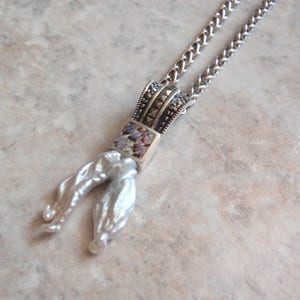 May include: A silver-toned necklace featuring a pendant with a rectangular abalone inlay and marcasite accents. The pendant is connected to a chain and has two large, white, baroque pearls hanging from it.