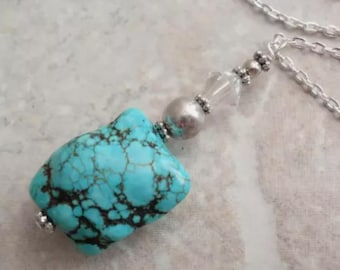 May include: A necklace featuring a rectangular turquoise pendant with dark brown matrix veining. The pendant is accented by a silver-toned bead, a clear faceted crystal bead, and small silver-toned spacers, all suspended from a silver-toned chain.
