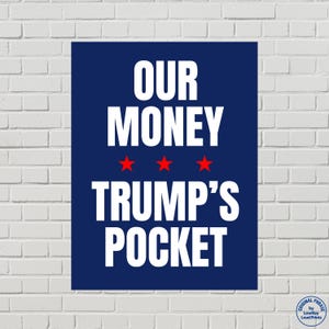 May include: A navy blue poster with white text that reads "OUR MONEY" above three red stars and "TRUMP'S POCKET". The poster is against a white brick wall. The phrase "ORIGINAL PHRASE by Lowkey Loud Prints" is in the bottom right corner.
