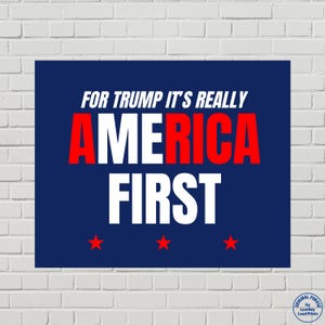 May include: A navy blue poster with white and red text that reads "FOR TRUMP IT'S REALLY AMERICA FIRST" with three red stars at the bottom. The poster is against a white brick wall.