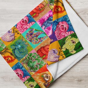 May include: A soft throw blanket featuring a vibrant patchwork design of colorful sloths. Each square displays a sloth in various artistic styles, including bright shades of pink, blue, green, orange, and yellow. The blanket has a white underside.