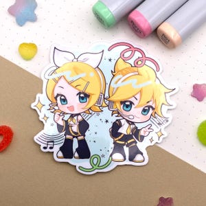 May include: A sticker featuring two anime-style characters with yellow hair and blue eyes. They wear black and gold outfits and have microphones. The background is light blue with musical notes and stars. The sticker is surrounded by colorful embellishments.