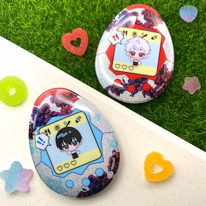 Puede incluir: Dos juguetes digitales con forma de huevo con diseños de personajes de anime. Los juguetes tienen un acabado plateado brillante, con detalles en rojo, morado y azul. Las pantallas muestran personajes de dibujos animados e iconos. Caramelos en forma de corazón y estrella están dispersos.