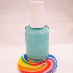 May include: A teal nail polish bottle with a white cap rests on a colorful, rainbow-swirled coaster. The coaster features a vibrant array of colors, including red, orange, yellow, green, blue, and purple. The nail polish bottle is clear, showcasing the teal color.
