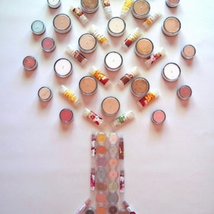 Könnte beinhalten: Eine Sammlung runder, cremefarbener Make-up-Behälter, die in Form eines Baumes angeordnet sind. Die Behälter sind von kleinen, runden, bunten Behältern umgeben. Am unteren Rand des Bildes befindet sich ein größerer Behälter, der 24 kleinere, runde, bunte Behälter enthält.