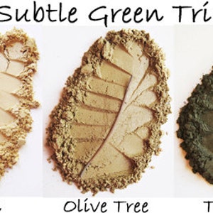 May include: The image displays three eyeshadow shades: Cornsilk, Olive Tree, and Tarnished. Each shade is arranged in a leaf shape, with a real leaf or stem accentuating the design. The text "Subtle Green Trio" is at the top.