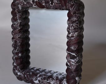 May include: A square mirror with a decorative frame. The frame has a twisted rope design and is a mix of dark red and white colors. The mirror is set against a white background.