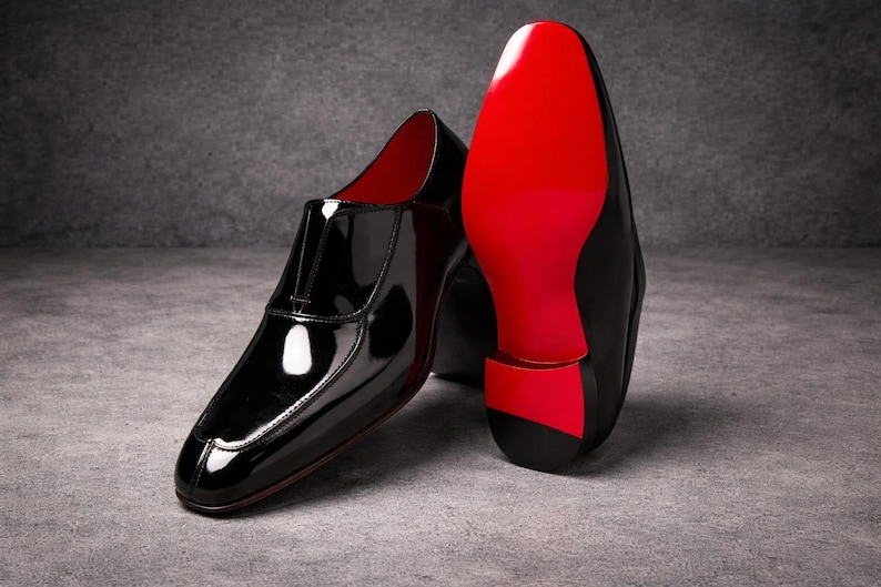 May include: A pair of black patent leather slip-on shoes with a striking red sole. The shoes have a glossy finish and a low-profile design, showcasing a modern aesthetic. The red sole provides a bold contrast.