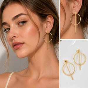 May include: A pair of gold-toned earrings featuring a circular hoop design bisected by a vertical bar that extends slightly beyond the top and bottom of the circle. The earrings have a smooth, matte finish and are shown worn on an earlobe.