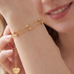 Dainty 18K gold beaded bracelet worn on woman's wrist by sunny window