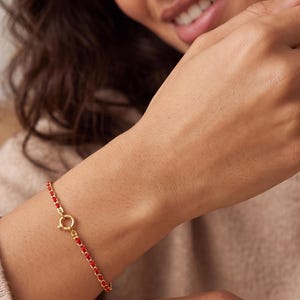 May include: A delicate gold chain bracelet featuring small, vibrant red beads spaced evenly along the length. The bracelet is secured with a circular spring ring clasp, showcasing a minimalist design that rests comfortably on the wrist.