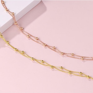 Two 18K rose gold Starry Sky bracelets layered on pink background