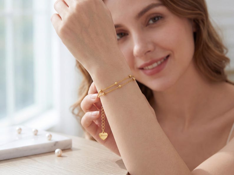Dainty 18K gold beaded bracelet worn on woman's wrist by sunny window