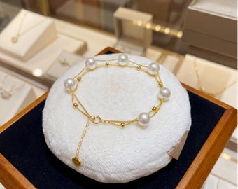 May include: A delicate double-strand gold bracelet featuring six evenly spaced white pearls and small gold beads. The bracelet includes a thin gold chain extension with a small heart-shaped charm at the end and a circular spring ring clasp.