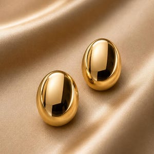 May include: A pair of polished gold-tone earrings with a smooth, rounded, oval-shaped design. The earrings feature a highly reflective, metallic surface that catches the light, creating distinct highlights and shadows across their curved forms.