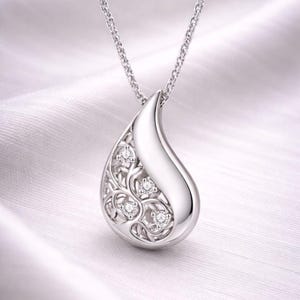 May include: A silver teardrop pendant necklace. The pendant features a polished, curved design with an openwork floral pattern on one side, set with small, sparkling gemstones. The necklace hangs on a delicate chain.