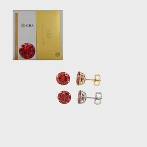 May include: Two pairs of stud earrings with round, red gemstones. One pair has gold-colored posts and backings, and the other has silver-colored posts and backings. A GRA certificate is in the background.