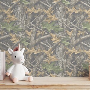 Puede incluir: Un unicornio de peluche blanco con cuerno y pezu&ntilde;as rosas est&aacute; sobre una superficie de madera. Detr&aacute;s hay varios libros con t&iacute;tulos como "UNICORNS" y "EARTH". El fondo presenta un patr&oacute;n de camuflaje marr&oacute;n, verde y beige.