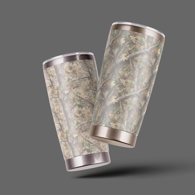 May include: Two stainless steel insulated tumblers with a camouflage pattern. The tumblers have a silver rim and base, and a lid. The camouflage design features shades of brown, green, and tan, resembling a forest scene.