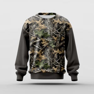 Puede incluir: Sudadera de cuello redondo con un dise&ntilde;o de camuflaje de corteza de &aacute;rbol y hojas en tonos marr&oacute;n, verde y gris. Las mangas son de color gris oscuro liso, y la sudadera tiene un dobladillo y pu&ntilde;os de canal&eacute;. Adecuada para actividades al aire libre.