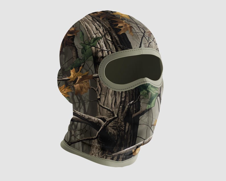 May include: A camouflage balaclava with a woodland pattern featuring brown, green, and tan hues. The balaclava has an oval eye opening and a light green trim. The fabric design mimics tree bark and fallen leaves.