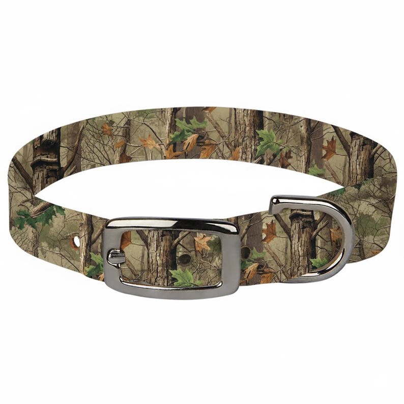 May include: Camouflage dog collar with a silver-colored buckle and D-ring. The collar features a realistic forest pattern with brown, green, and tan hues. The collar is designed for pets.