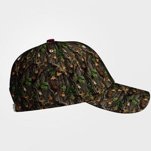 May include: A camouflage baseball cap with a curved brim. The cap features a pattern of brown, green, and tan leaves and branches. The top button is a dark red color.