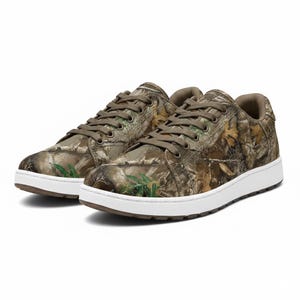 May include: A pair of low-top sneakers featuring a camouflage pattern in shades of brown, green, and tan. The shoes have white soles and brown laces. The design incorporates a realistic forest print.