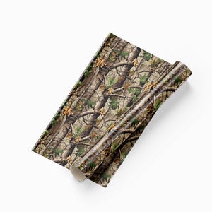 May include: A roll of camouflage pattern material. The pattern features a mix of brown, green, and tan colors, resembling a forest environment with branches and leaves. The material is partially rolled, revealing the pattern.