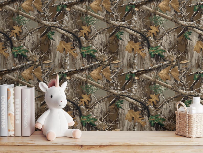 May include: A white unicorn plush toy with a pink horn and hooves sits on a wooden surface. Behind it is a camouflage pattern wallpaper with brown, green, and tan tones. Books and a small basket are also on the surface.