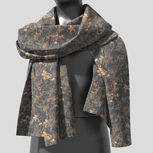 May include: A dark gray scarf with a repeating pattern of tan and brown leaves and foliage. The scarf is draped over a mannequin, showcasing its design and texture. The scarf appears to be made of a soft, flowing fabric.