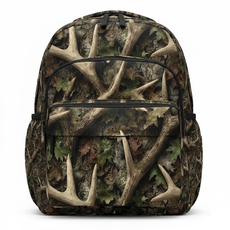 Puede incluir: Mochila de camuflaje con un patr&oacute;n de cornamentas y hojas en tonos marr&oacute;n, verde y beige. La mochila tiene m&uacute;ltiples compartimentos con cremallera y la espalda acolchada.