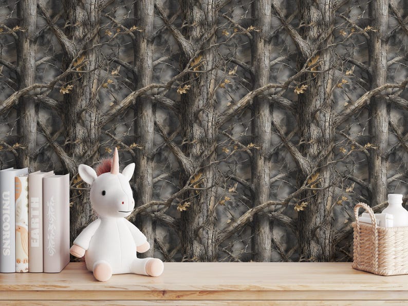 Puede incluir: Un juguete de peluche de unicornio blanco con cuerno y pezu&ntilde;as rosas est&aacute; sobre una superficie de madera. Detr&aacute;s, un papel pintado con un patr&oacute;n de camuflaje de troncos y ramas de &aacute;rboles. Tambi&eacute;n hay libros y una peque&ntilde;a cesta.