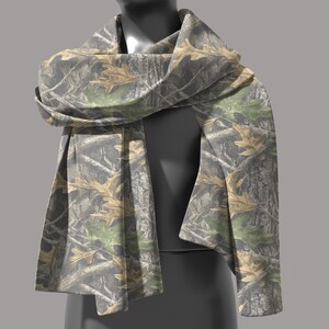 Puede incluir: Bufanda de camuflaje con un patr&oacute;n de hojas y ramas marrones, verdes y grises. La bufanda est&aacute; drapeada sobre un maniqu&iacute;, mostrando su dise&ntilde;o y textura. La tela parece suave y ligera.