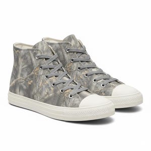 May include: A pair of high-top sneakers with a camouflage pattern in shades of gray, brown, and beige. The sneakers have gray laces, white rubber soles, and white toe caps. The shoes are designed for casual wear.