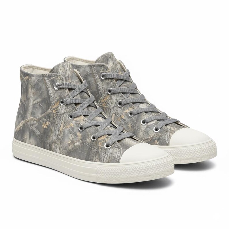 May include: A pair of high-top sneakers with a camouflage pattern in shades of gray, brown, and beige. The sneakers have gray laces, white rubber soles, and white toe caps. The shoes are designed for casual wear.
