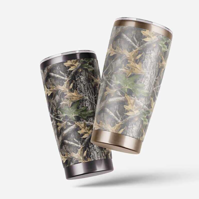 Puede incluir: Dos vasos aislados con un dise&ntilde;o de camuflaje en tonos marrones, verdes y beige. Los vasos tienen un borde y una base de acero inoxidable. El dise&ntilde;o se asemeja a un bosque con hojas y corteza de &aacute;rbol.