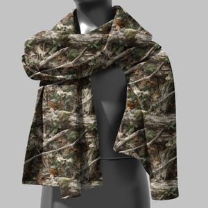 Puede incluir: Bufanda de camuflaje con un patr&oacute;n forestal realista. El dise&ntilde;o presenta corteza de &aacute;rbol marr&oacute;n, hojas verdes y ramas, creando una est&eacute;tica natural al aire libre. La bufanda est&aacute; drapeada sobre un maniqu&iacute;.