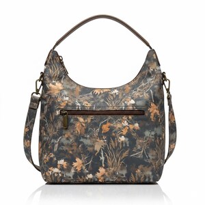 May include: A shoulder bag with a camouflage pattern featuring brown, tan, and green leaves and foliage. The bag has a brown handle and a detachable shoulder strap. A zipper pocket is visible on the front.