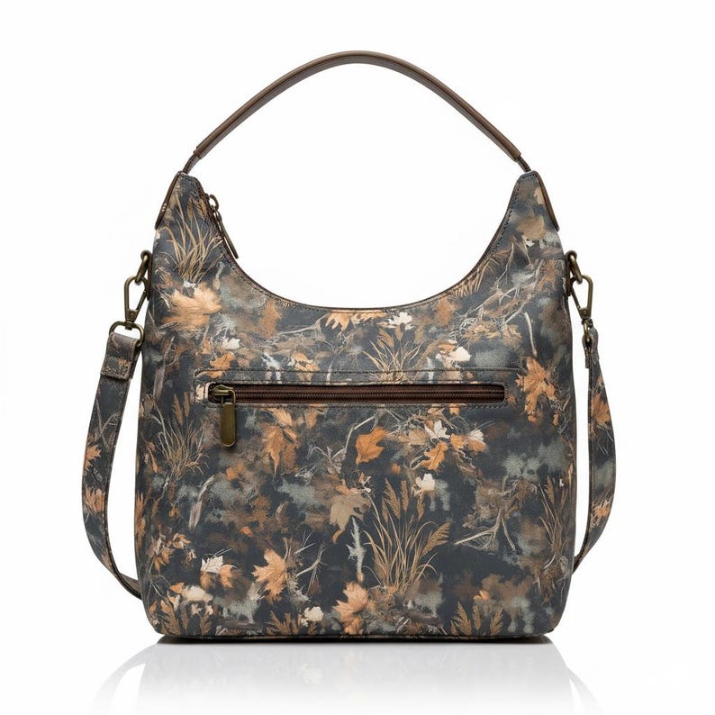May include: A shoulder bag with a camouflage pattern featuring brown, tan, and green leaves and foliage. The bag has a brown handle and a detachable shoulder strap. A zipper pocket is visible on the front.