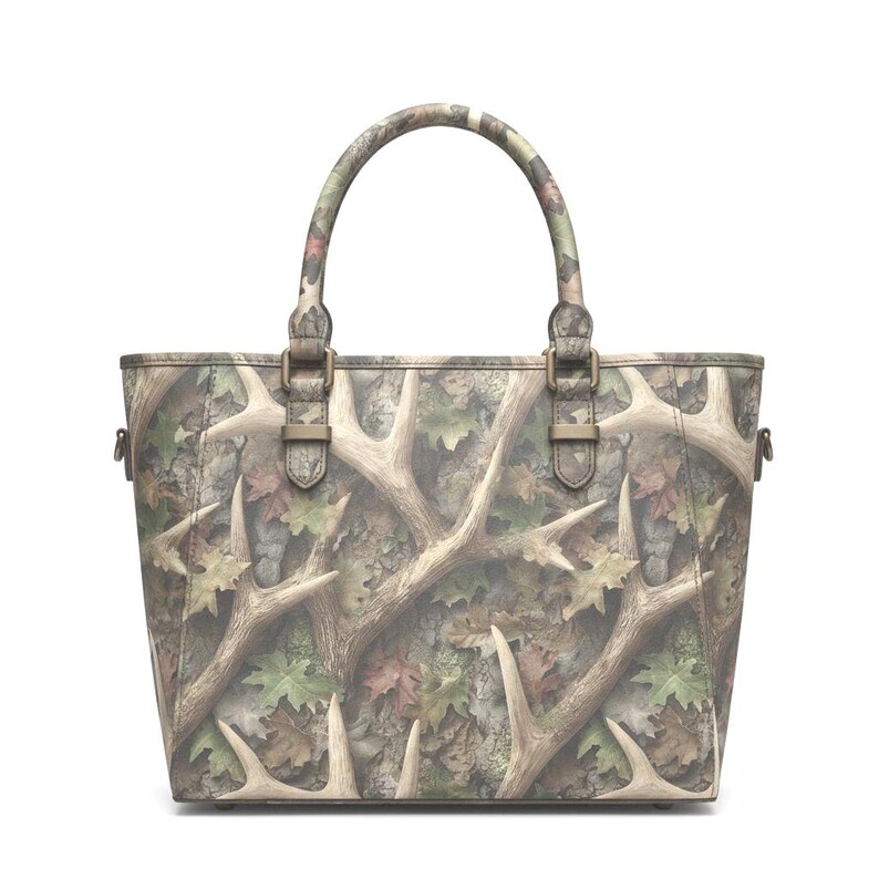 May include: A camouflage tote bag with a brown and green pattern featuring deer antlers and leaves. The bag has a top handle and metal hardware. The bag is designed with a shoulder strap.