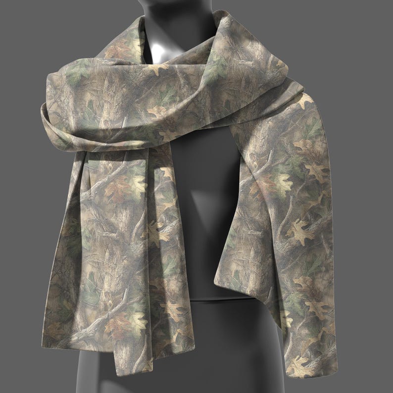 May include: A camouflage-patterned scarf draped over a mannequin. The scarf features a mix of brown, green, and tan hues, with a detailed print of leaves and branches. The fabric is soft and appears to be lightweight.