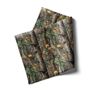 May include: Two folded fabric squares with a camouflage pattern. The design features a blend of brown, green, and yellow hues, mimicking a forest environment. The fabric appears to be a medium weight material.