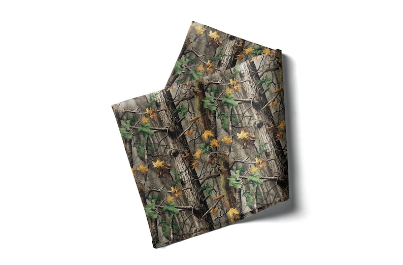 May include: Two folded fabric squares with a camouflage pattern. The design features a blend of brown, green, and yellow hues, mimicking a forest environment. The fabric appears to be a medium weight material.
