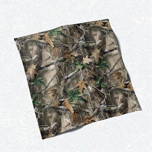 May include: A folded textile featuring a camouflage pattern. The design incorporates realistic depictions of tree bark, branches, and leaves in shades of brown, green, and tan. The fabric appears to be soft and flexible, suitable for various applications.