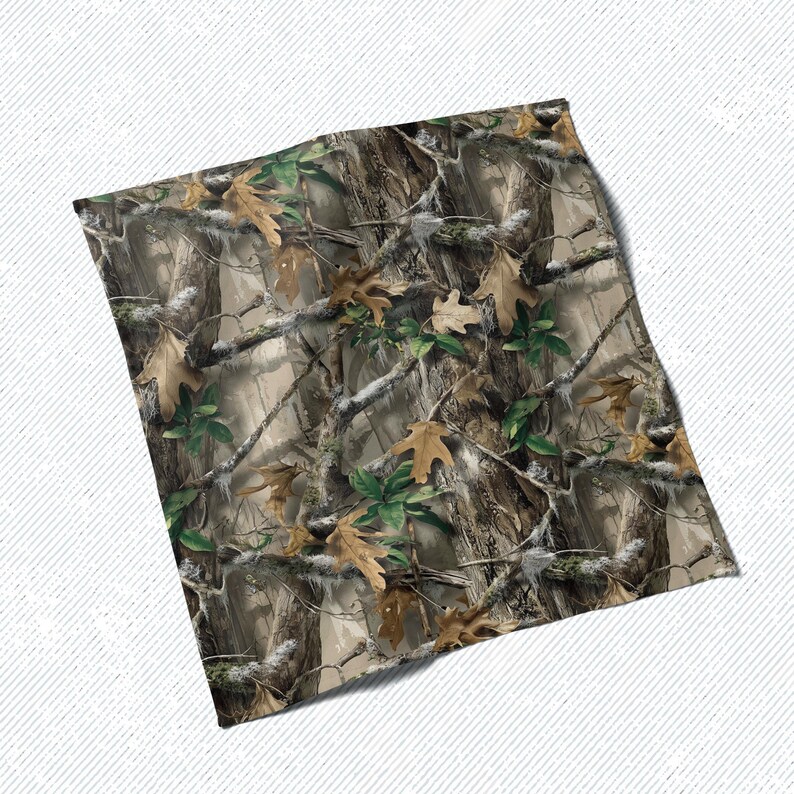 May include: A folded textile featuring a camouflage pattern. The design incorporates realistic depictions of tree bark, branches, and leaves in shades of brown, green, and tan. The fabric appears to be soft and flexible, suitable for various applications.