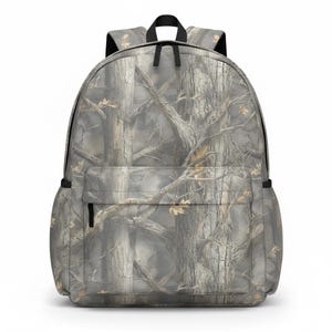 May include: A gray and brown camouflage backpack with a front pocket and black zippers. The backpack features a top handle and adjustable shoulder straps. The pattern resembles a forest scene with tree trunks and branches.